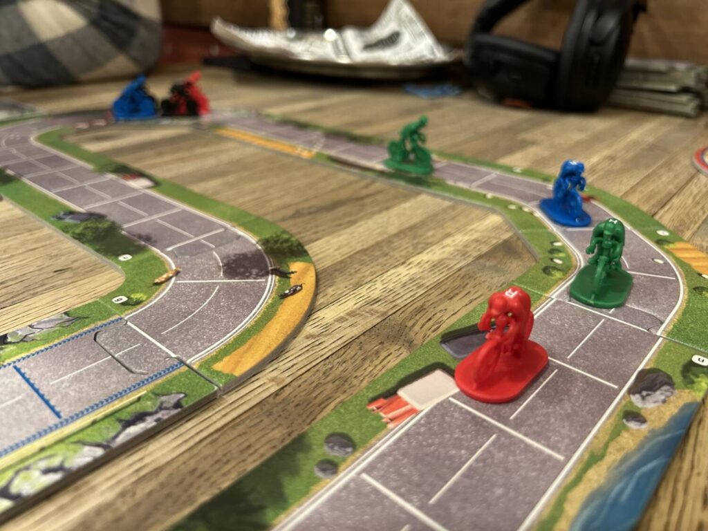 Cyclists race around a track corner. More racers can be seen off in the distance.