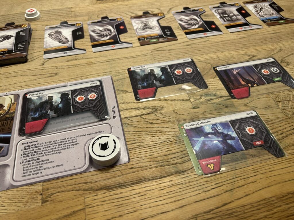 A player board, three Threat Cards, and a row of Upgrade cards on a wooden table.