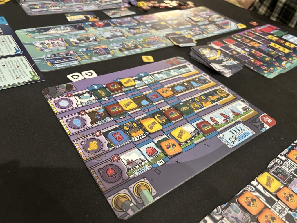 A rectangular board with four tracks, each covered in illustrations, sits on a table with a black neoprene mat.