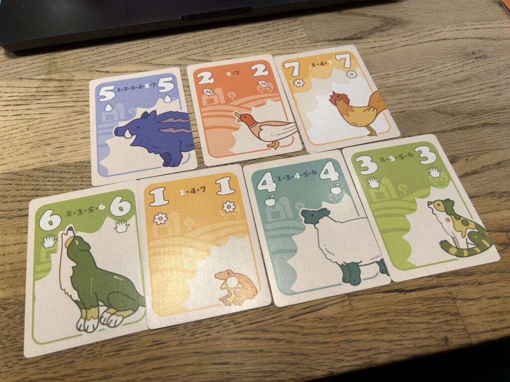 One of each value of card for Farm Hand sits on a wooden table. Each card has a bold, colorful illustration of a farm animal.