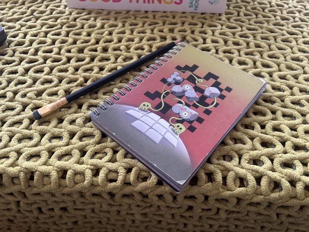 A spiral bound notebook sits on a table next to a black pencil.