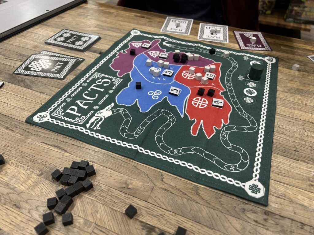 A square, green cloth board sits on a wooden table. The map, a rough outline of Ireland, is divided into six regions. Each contains a number of cubes and scoring tiles.
